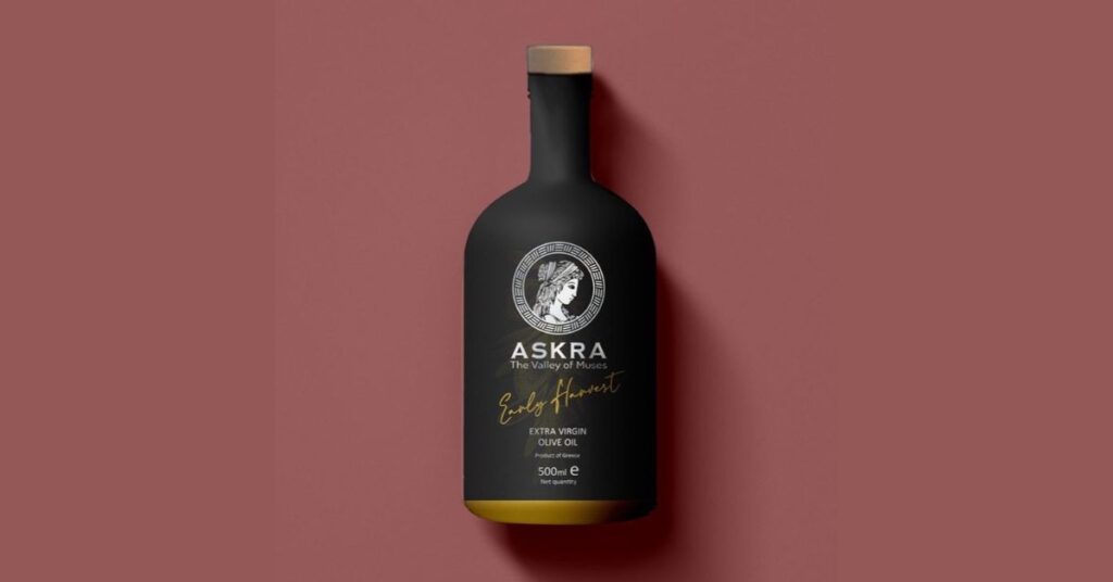 A bottle of Askra Extra Virgin Olive Oil, featuring elegant gold and green labeling, set against a natural backdrop inspired by the Valley of the Muses in Greece.